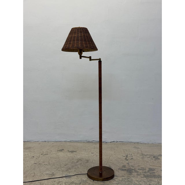 Rattan wrapped mid-century floor lamp with a brass base, adjustable arm and a wicker shade circa 1960s.
