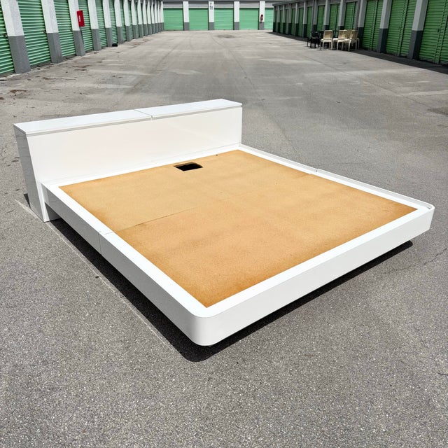 A sleek postmodern king size platform bed featuring a high-gloss white laminate finish and softly rounded edges. The low-...
