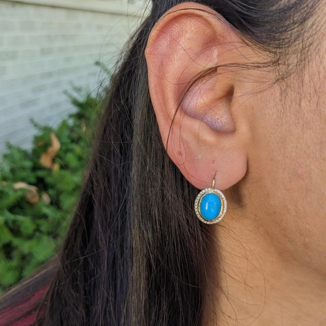 This elegant earring features a pair of 5.32 carat Sleeping Beauty Turquoise gemstones with a halo of natural earth mined...