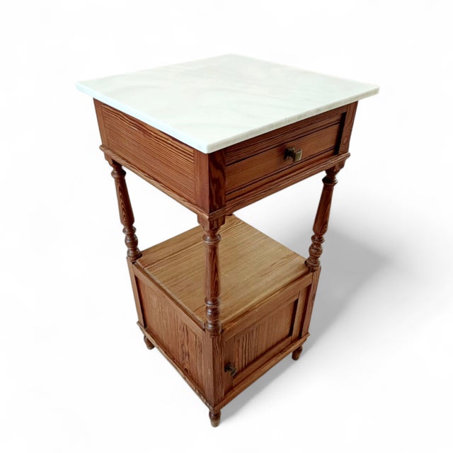 A French 1940s nightstand, expertly crafted in richly grained solid oak and crowned with a pristine white marble top inset...