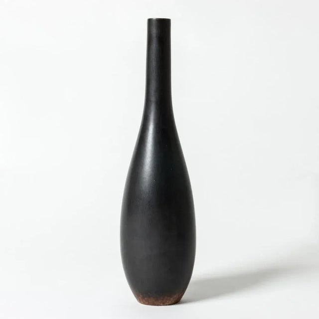 Striking stoneware vase by Carl-Harry Stålhane in a narrow, drop-shaped form. Jet black glaze with rusty color around the...