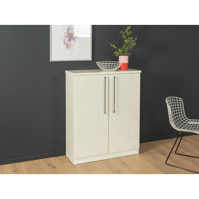 Classic chest of drawers from the 1990s. High-quality body in white-stained ash veneer with two shelves and two doors with...