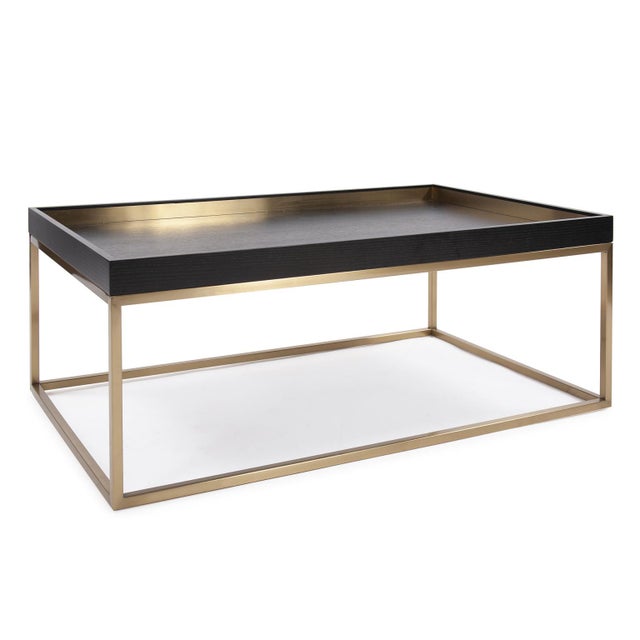 The Vassio Coffee Table features a tray top design in an ebony wood veneer accented with metal touches in brushed brass....