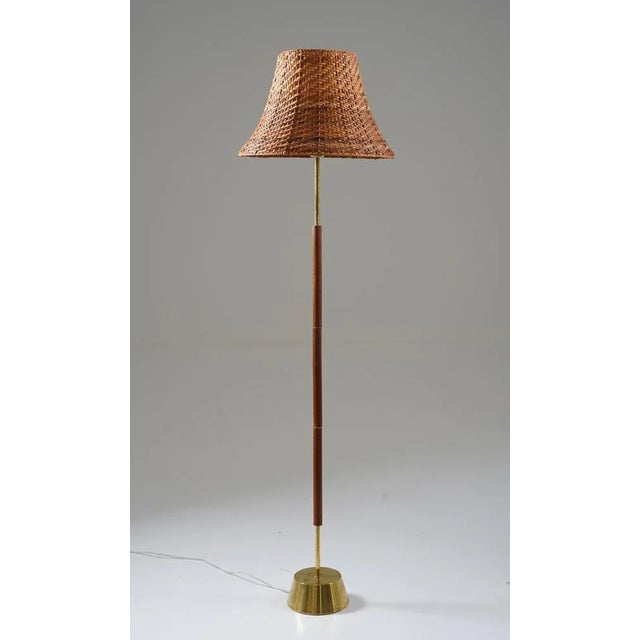 Simple and elegant floor lamp in teak and brass by Boréns, Sweden. The lamp features a heavy brass base, supporting a rod...
