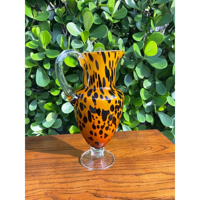Striking vintage art glass pitcher featuring a bold leopard spot pattern in rich amber and black tones. The elegant...