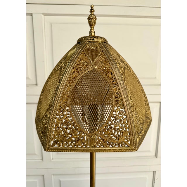 Here is an elegant tiered wood floor lamp featuring an exceptionally ornate gold-tone metal filigree shade, dating to the...