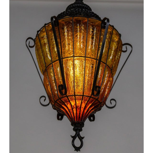 An amber, crackle, caged glass lantern pendant light from the mid 20th century; in an elegant shape with a decorative cap...