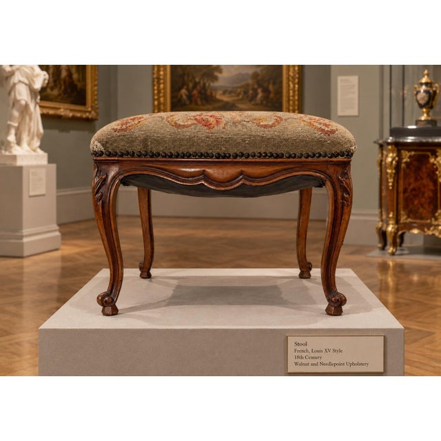 This is a low wooden footstool featuring a curvilinear carved apron and cabriole legs ending in scroll feet. The over-...
