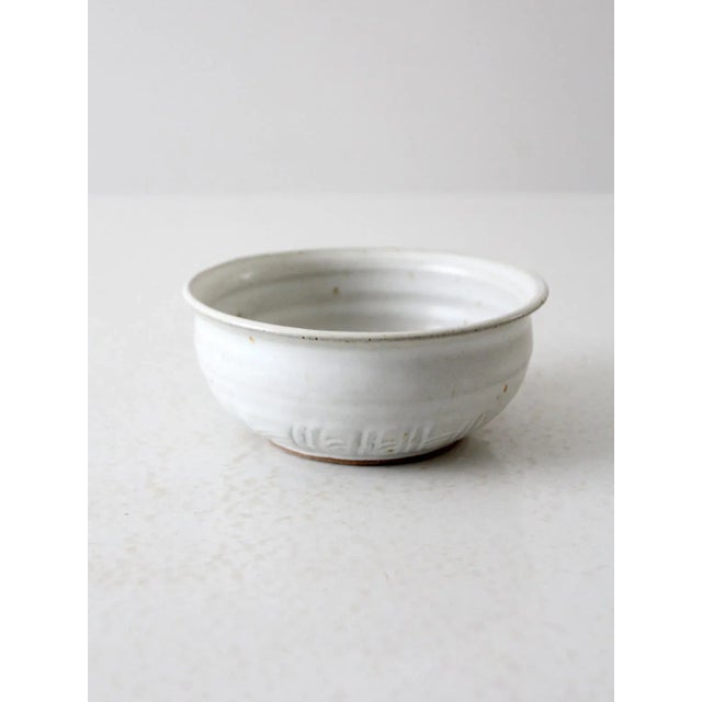 This is a vintage handmade studio pottery bowl. The white speckled glaze bowl has a subtle etched design around the base...