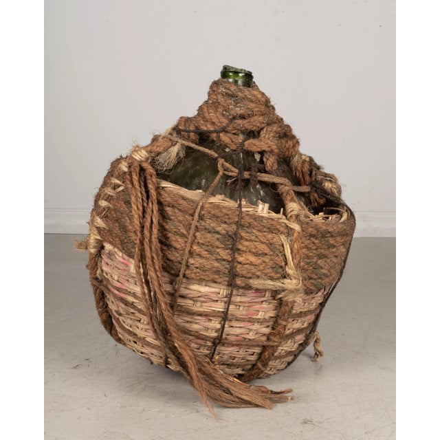 A large 19th century French globular form hand blown green glass Dame Jeanne, or demijohn, bottle encased in two layers of...