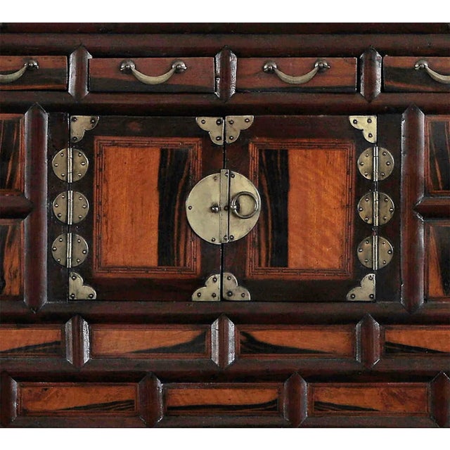 Vintage Asian cabinet featuring contrasting dark wood. The chest features four small drawers at the top, a double-door...