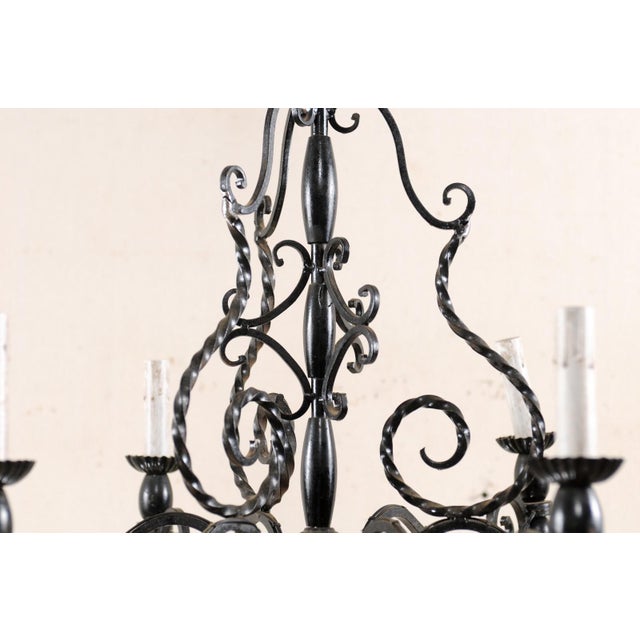A French scrolling iron six-light chandelier from the mid 20th century. This French vintage chandelier is adorned with...