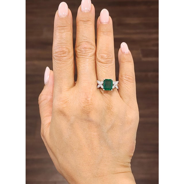 This exquisite ring showcases a 2.83-carat emerald-cut emerald, radiating a vibrant green hue. Flanked by marquise-cut...