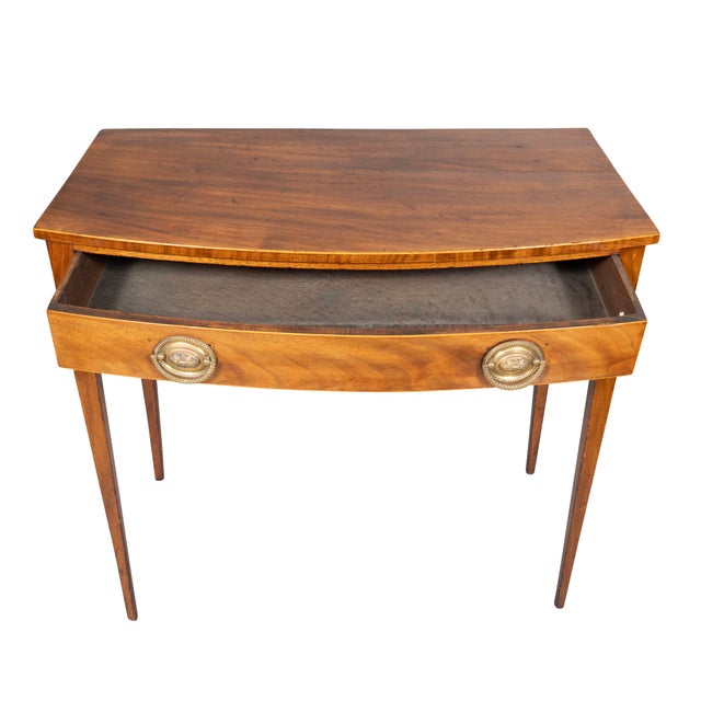 Rectangular bowed top over a drawer with oval brass handles. Square tapered legs.