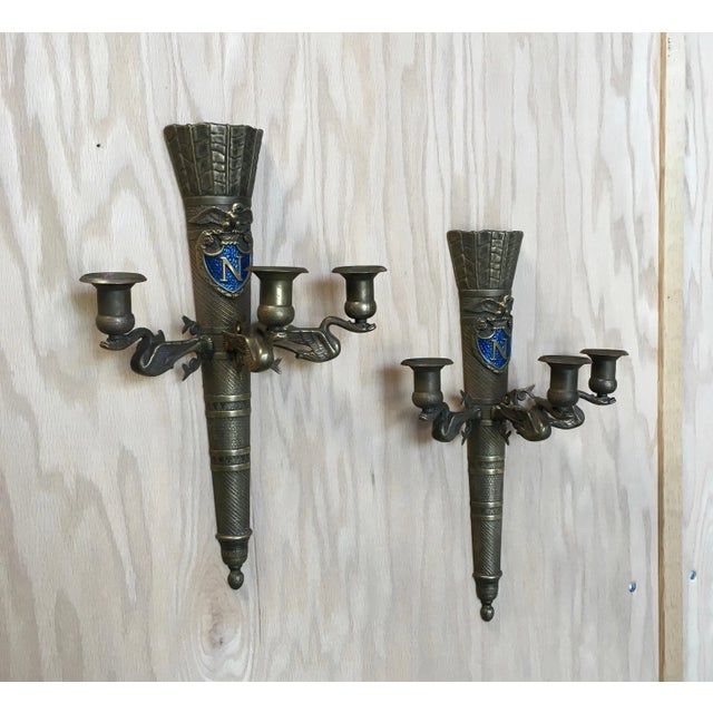 Pair of brass antique neoclassical Revival sconces with the royal blue Napoleon symbol. Wear consistent with age and use.