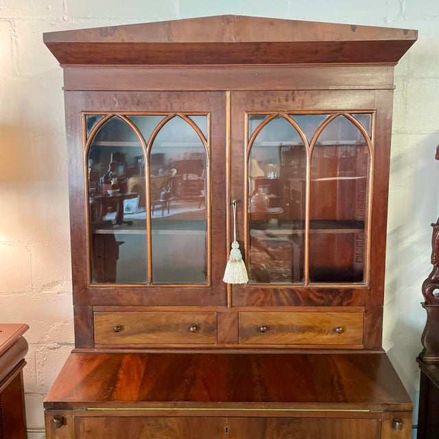 Antique American flame mahogany secretary bookcase in the Sheraton style featuring an upper cupboard with three shelves...