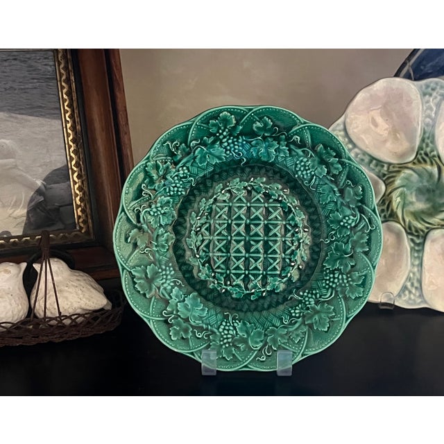 Green wedgwood wall plate decorated with a criss cross pattern in the middle surrounded by grapes and leaves.