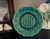 Green wedgwood wall plate decorated with a criss cross pattern in the middle surrounded by grapes and leaves.