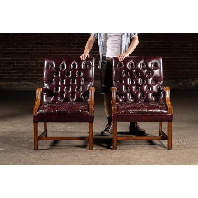 Stately pair of square-backed dining chairs upholstered in rich oxblood leather with classic deep button tufting and brass...