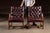 Stately pair of square-backed dining chairs upholstered in rich oxblood leather with classic deep button tufting and brass...