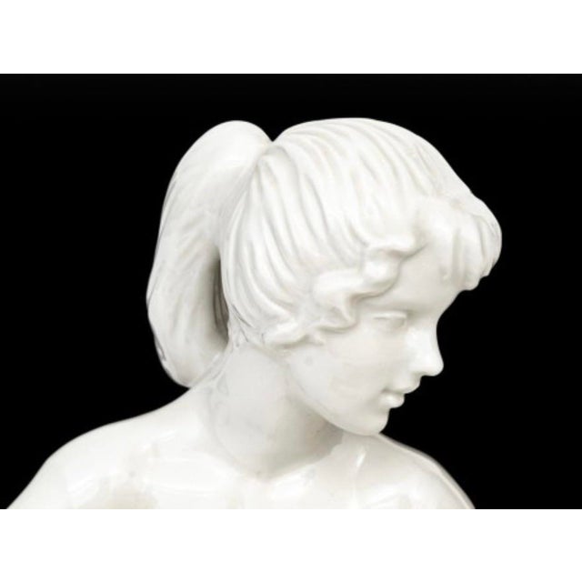 An elegant vintage German porcelain figurine depicting a seated nude female figure in a graceful twisting pose. Rendered...