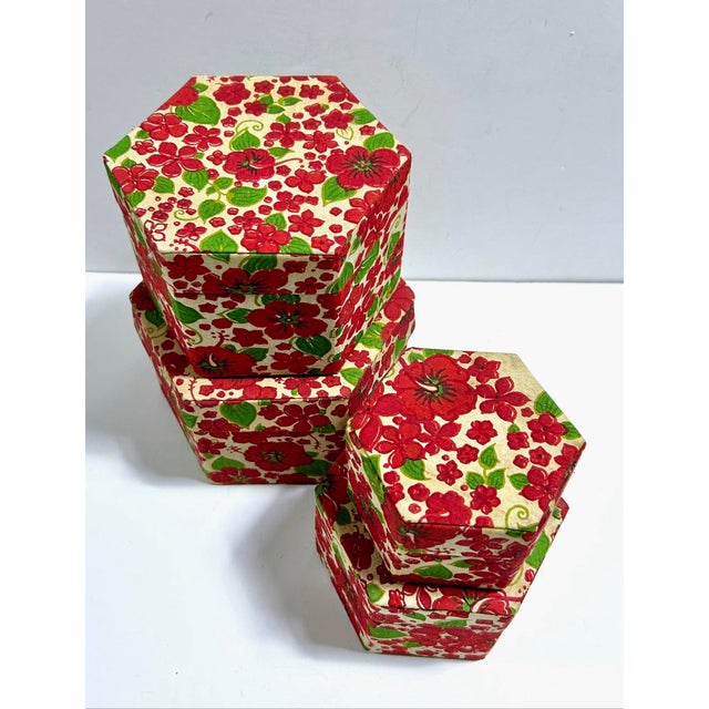 A striking set of four vintage nesting boxes covered in vivid red-and-green floral cotton textile. The graduated hexagonal...