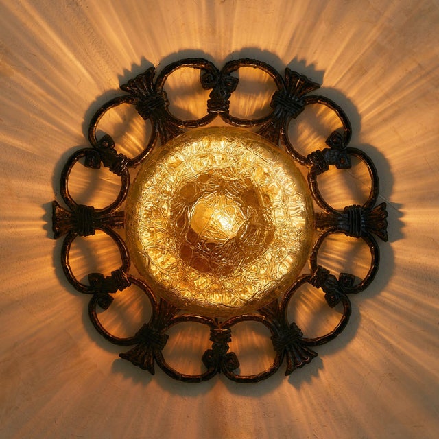 An Italian sconce from the 1970s, defined by its verdigris iron frame and molten amber glass dome. The hand-wrought iron...