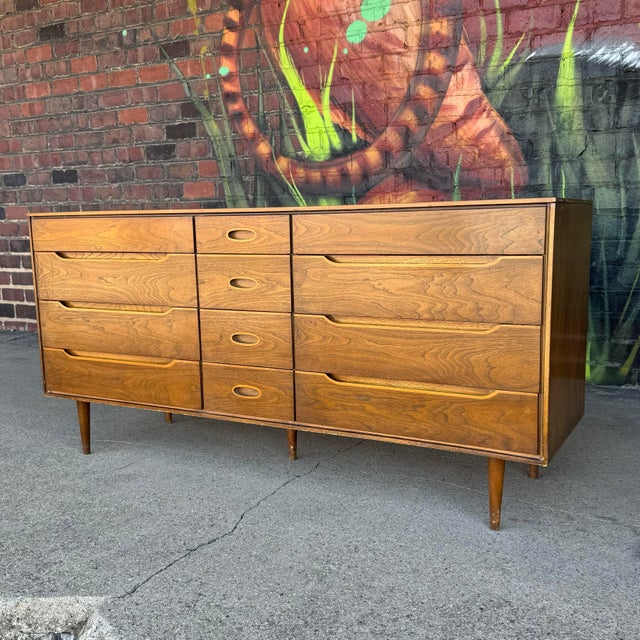 This wood dresser features a unique drawer configuration with contrasting wood tones along the drawer pulls. The maker is...