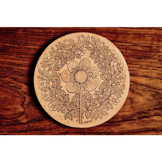 This circular ceramic plaque features a stylized floral composition with a central blossom surrounded by delicately...
