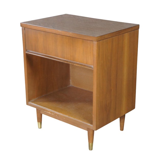 An antique 1960s Mid Century Modern Walnut night stand. Features a rectangular form with a laminate top and dovetailed...