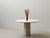 Sculptural dining table made of solid travertine with a round tabletop and a central, polygonal pedestal base. The...