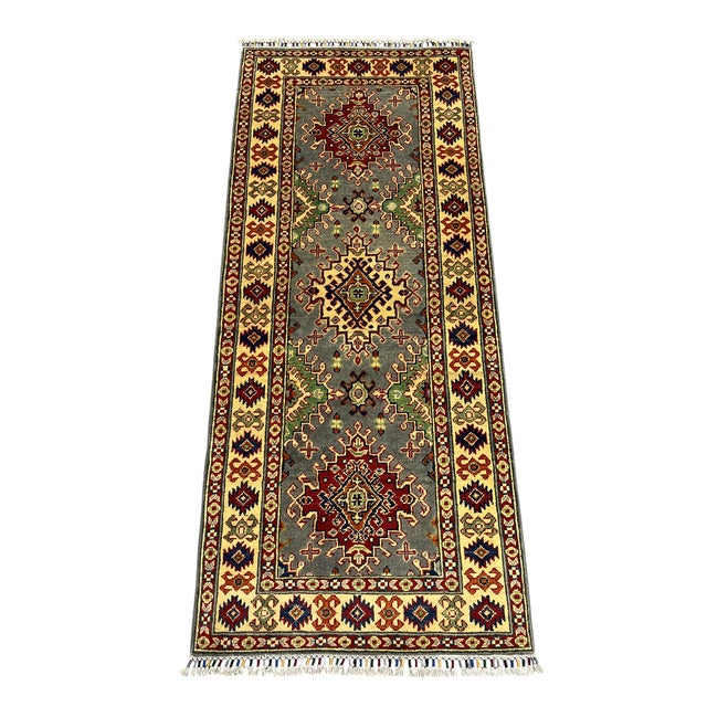 This Kazak-style wool runner features three bold tribal medallions on a gray field. A cream border frames the design, with...
