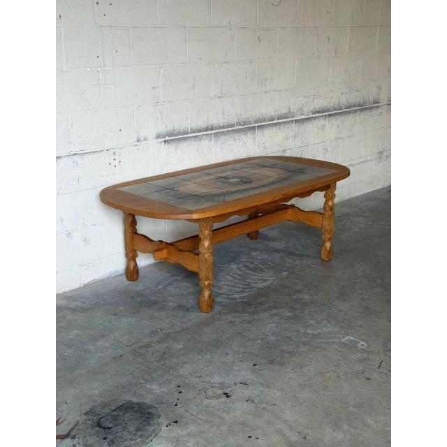 This oval coffee table features an inset ceramic tile top with an artistic radial motif. Sculpted legs and a stretched...