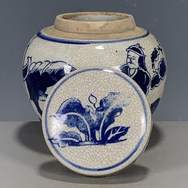 This round lidded jar features a classic crackle glaze cream ceramic body decorated with bold blue-and-white hand-painted...