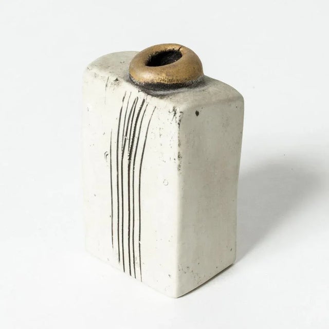 Small stoneware sculpture by Bengt Berglund in a boxy form with a striped decor and a gold glazed “mouth” on top. This...