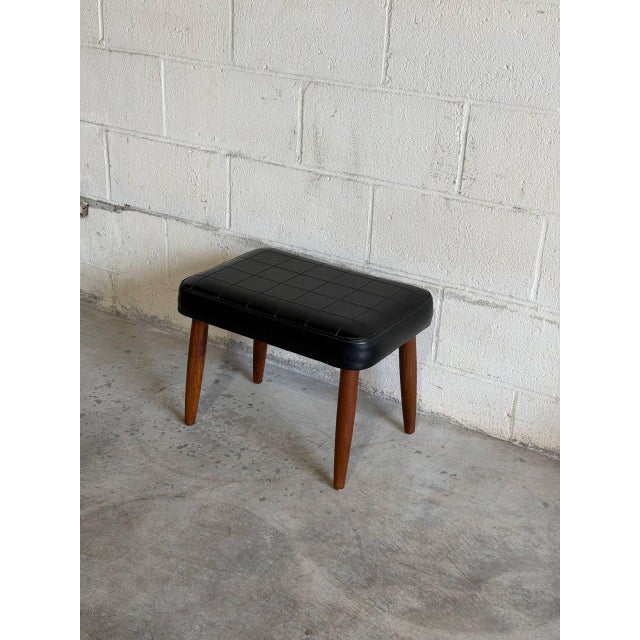 Vintage Danish modern ottoman featuring tapered teak legs and a black upholstered cushion with geometric tufted detailing....