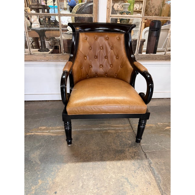 Handsome Regency-style armchair featuring caramel brown tufted leather, nailhead trim, and a dramatic ebonized wood frame....