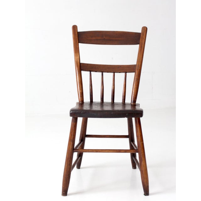 Antique primitive plank seat chair featuring a simple spindle back, gently curved rails, and slender turned legs. Rich...