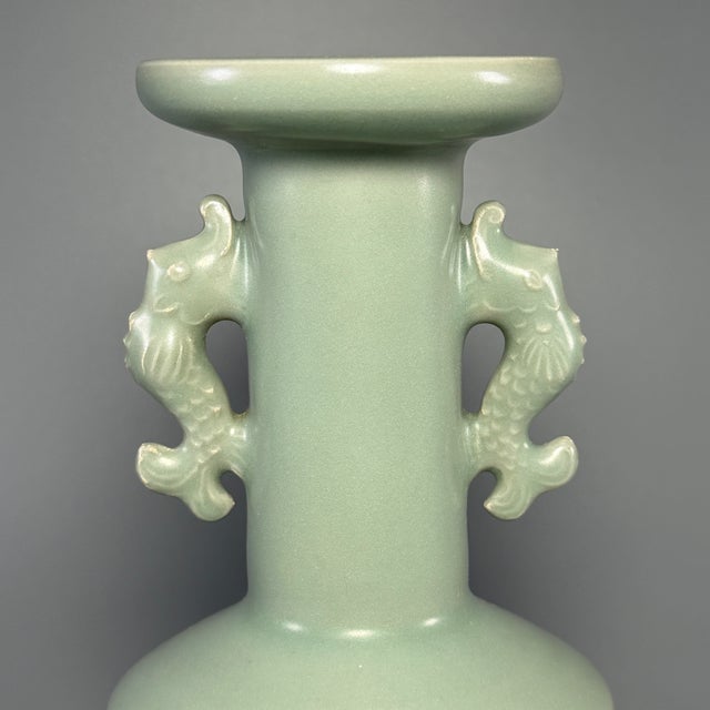 This elegant vessel is a classic Longquan celadon vase from China, decorated with a pair of vivid carp-shaped handles on...