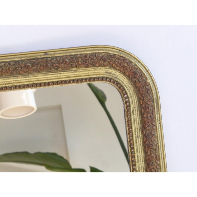 French antique Louis Philippe wall mirror with an ornate golden gilded frame with a floral pattern. The mirror is made in...