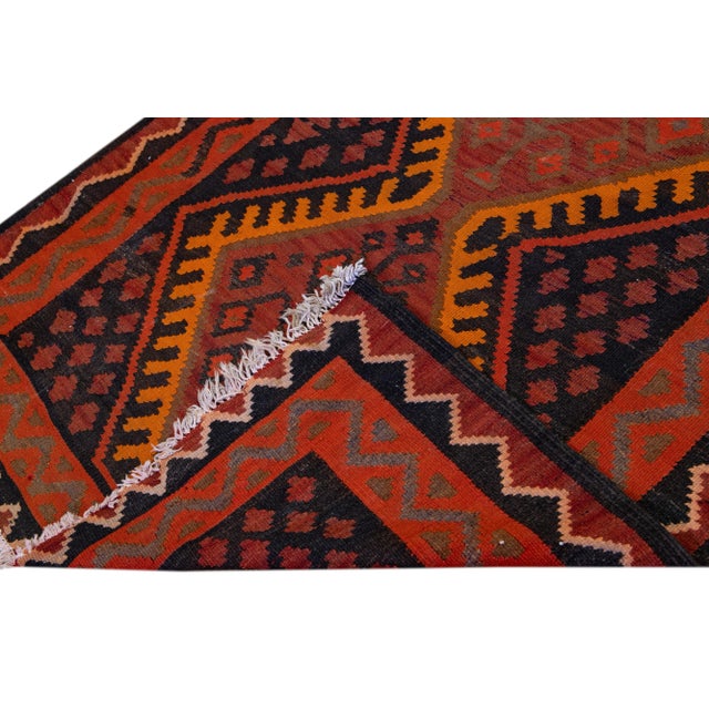 Beautiful kilim handmade wool runner with a brick-red field. This Vintage flatweave rug has orange, black, and brown...