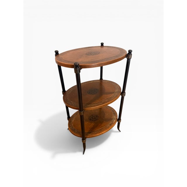 A handsome three-tier accent table featuring a warm brown leather-wrapped surface with decorative embossed borders and...