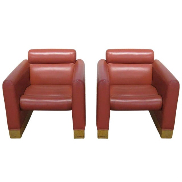 A pair of Karl Springer Style red faux leather club chairs. Featuring broad architectural arms, plush cylindrical back and...