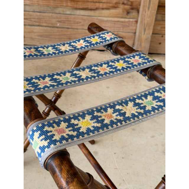 A charming vintage folding luggage rack featuring a warm faux bamboo frame and three colorful needlepoint support straps....