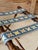 A charming vintage folding luggage rack featuring a warm faux bamboo frame and three colorful needlepoint support straps....