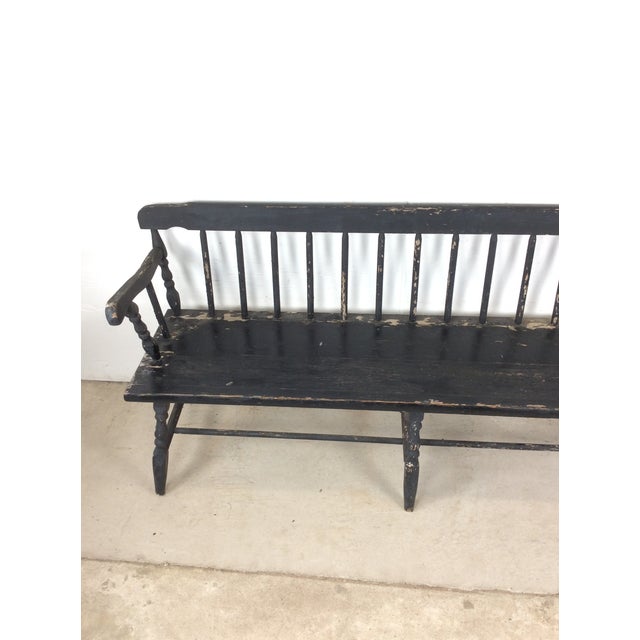 This antique Deacon's bench features hardwood construction, chippy black painted finish, sculpted arms, and stretcher base.