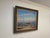 Framed oil painting depicting a serene coastal scene with sailboats, fishermen, and calm waters under a bright sky....