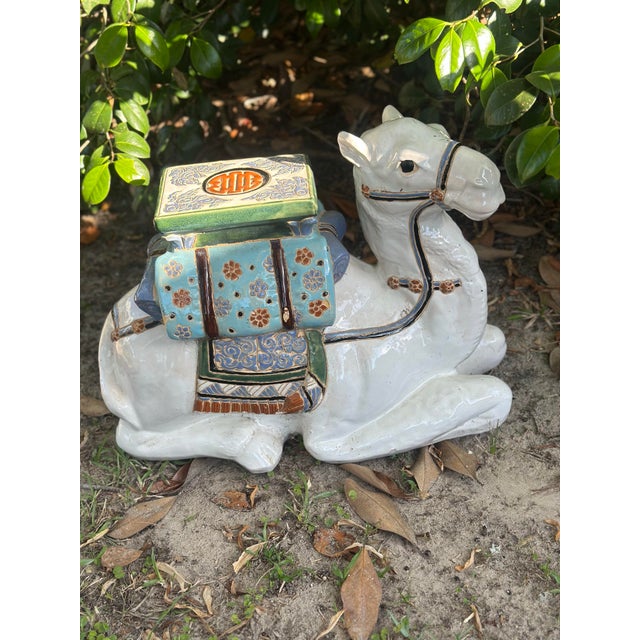 A striking ceramic garden stool sculpted in the form of a resting camel, richly decorated with hand-painted floral and...