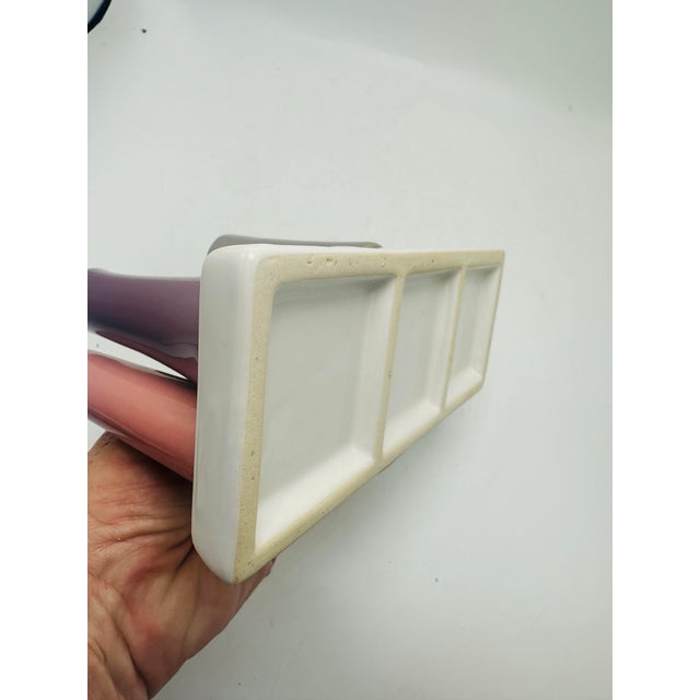 This is a ceramic art piece consisting of eight small, narrow, tubular vases in various colors mounted on a white...