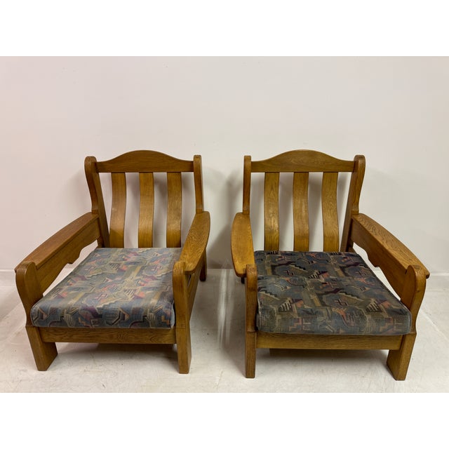 A pair of solid oak armchairs in a restrained Brutalist style, dating to the mid-20th century. The design combines robust...